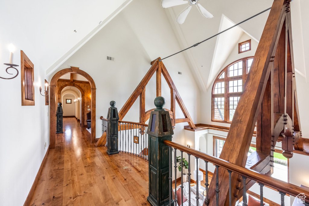 Hallway featuring an upstairs landing, high vaulted ceiling, arched walkways, wood-type flooring, and baseboards