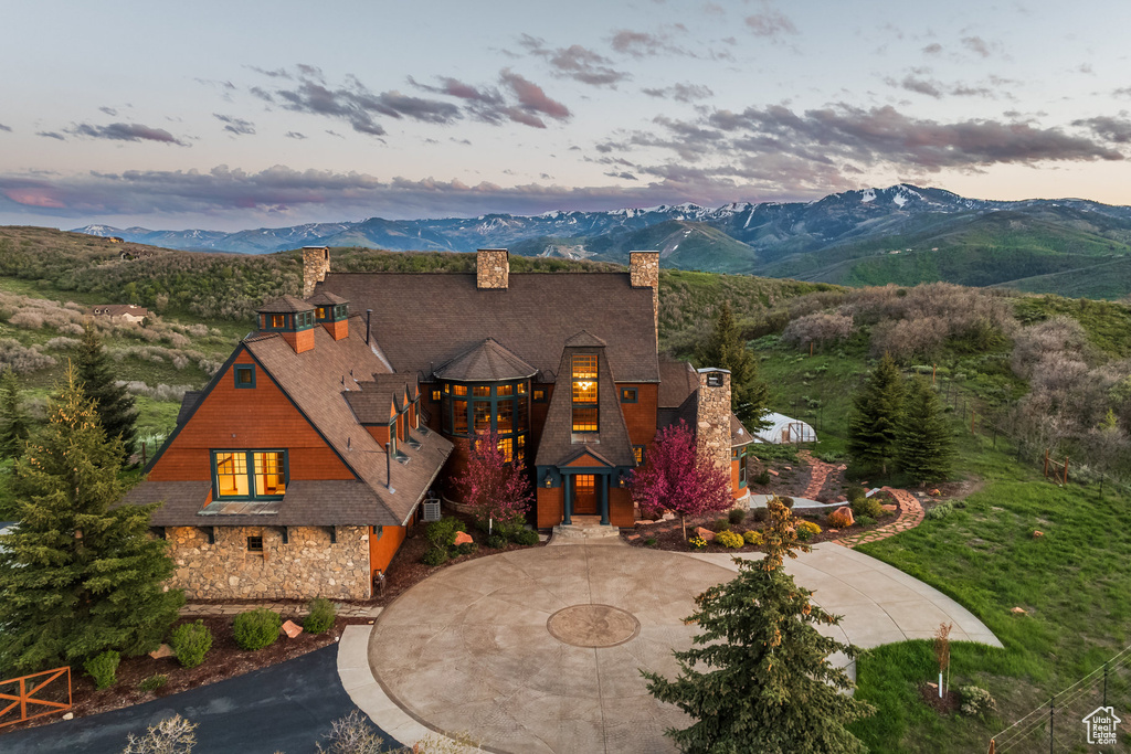 View of front facade with curved driveway, a chimney, stone siding, and a mountain view