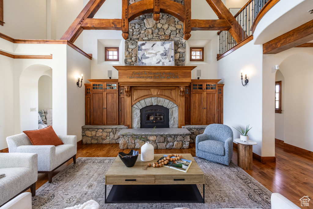 Living room featuring arched walkways, high vaulted ceiling, wood finished floors, baseboards, and a large fireplace