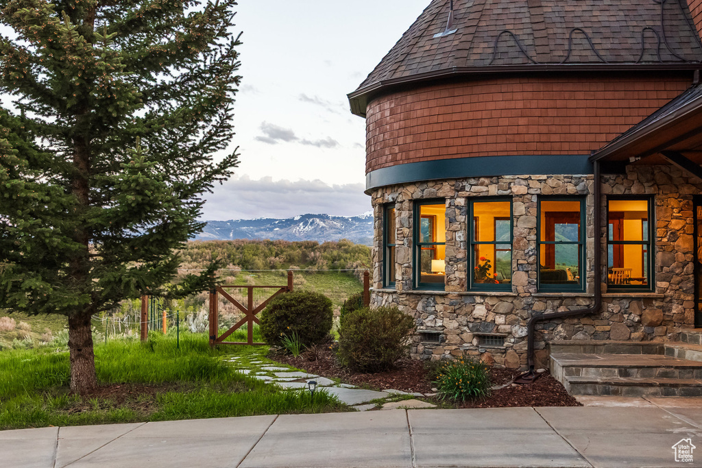 View of property exterior with stone siding, a mountain view, and a shingled roof
