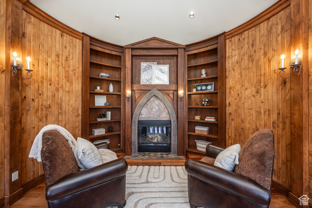 Living area with a tile fireplace, wood walls, built in shelves, wood finished floors, and baseboards