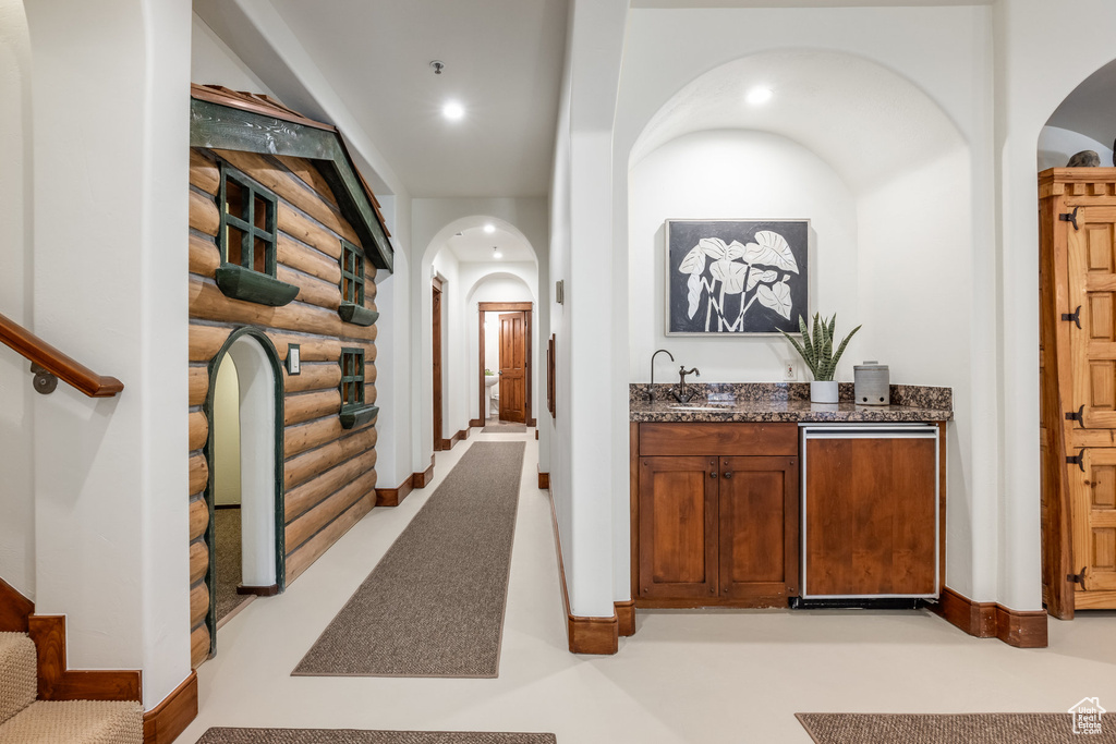 Hall with log walls, arched walkways, stairway, a sink, and baseboards