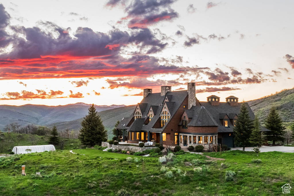 Back of house at dusk with a chimney, a yard, and a mountain view