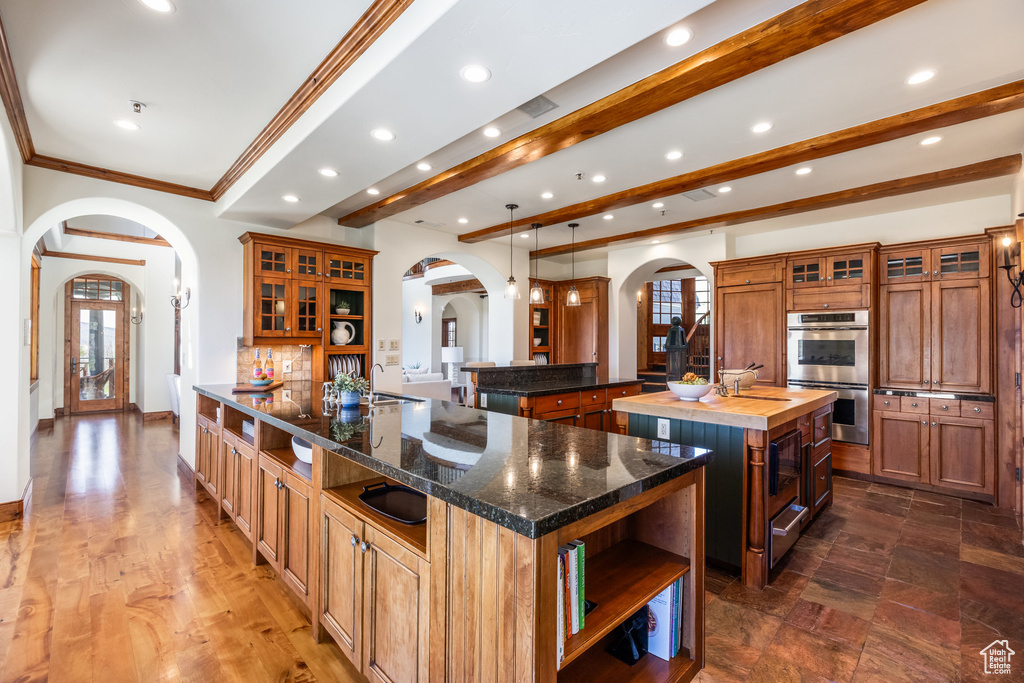 Kitchen with arched walkways, a spacious island, stainless steel double oven, open shelves, and recessed lighting