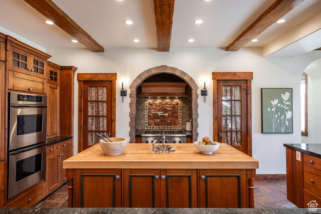 Kitchen with double oven, butcher block counters, beamed ceiling, stone tile floors, and recessed lighting