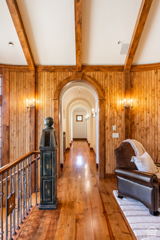 Corridor with beamed ceiling, wood walls, hardwood / wood-style floors, and arched walkways