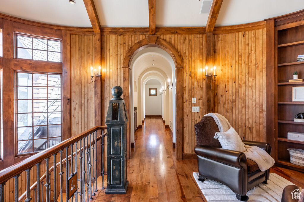 Hallway with wood walls, beam ceiling, an upstairs landing, wood finished floors, and arched walkways