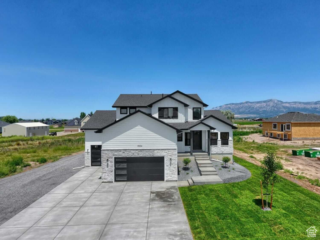 Modern inspired farmhouse with an attached garage, concrete driveway, a mountain view, stone siding, and a front yard