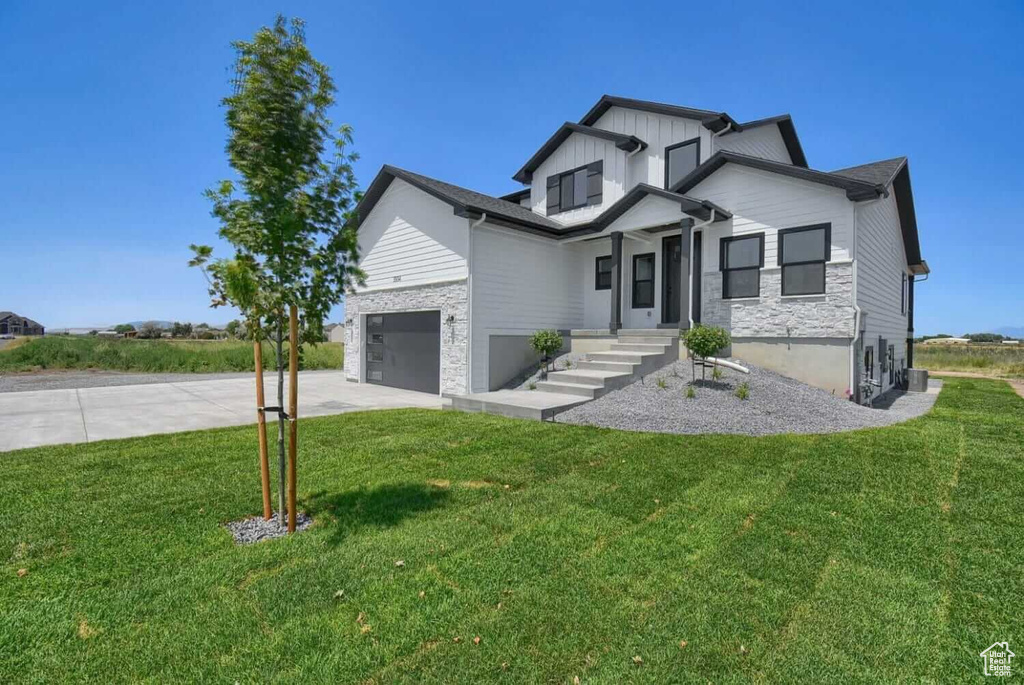 Modern inspired farmhouse featuring driveway, board and batten siding, a front yard, and stone siding