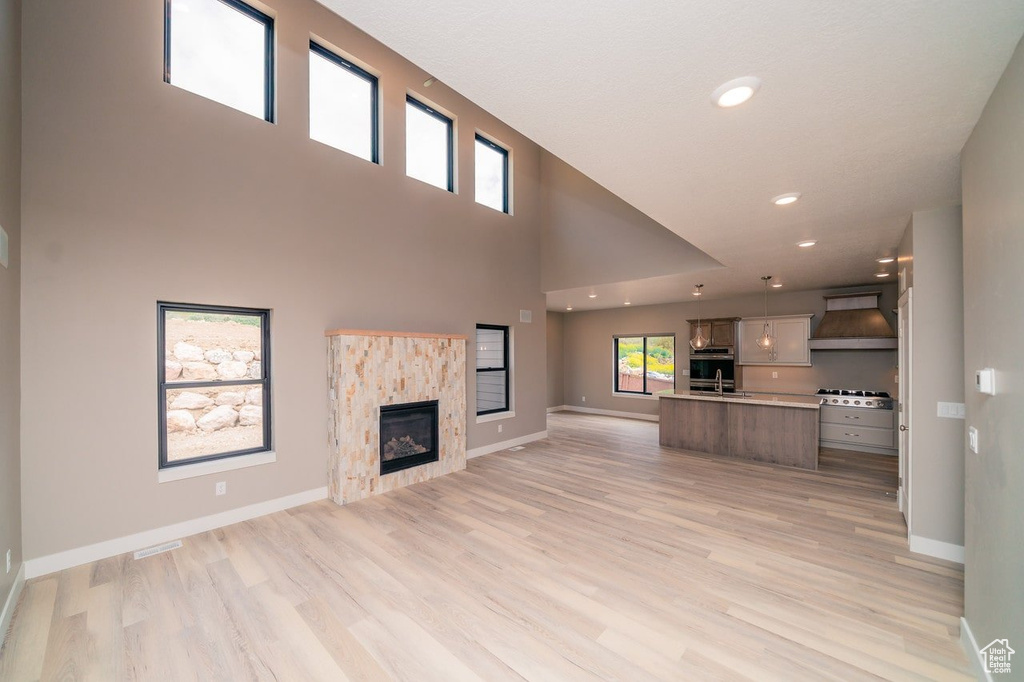 Unfurnished living room featuring light wood-type flooring, a tile fireplace, baseboards, a towering ceiling, and recessed lighting