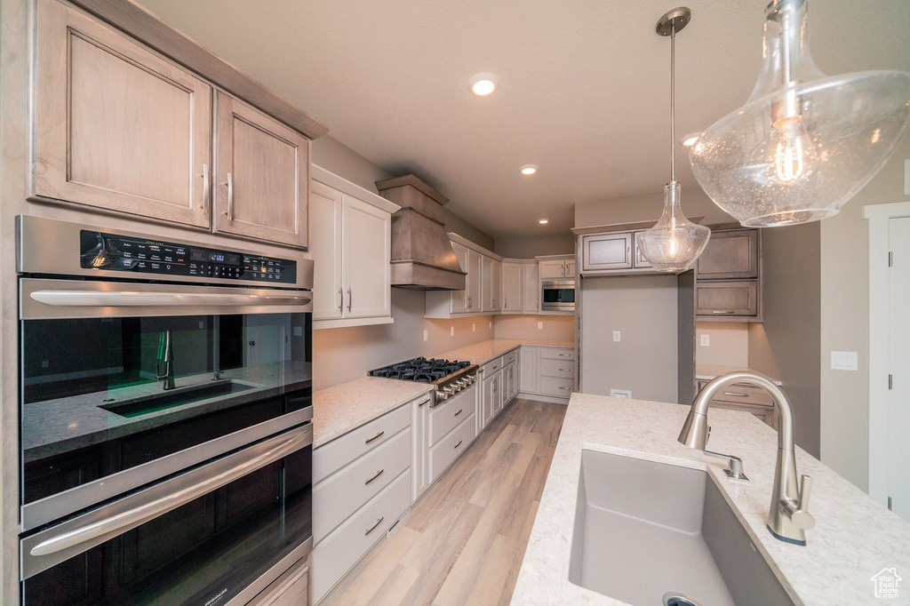 Kitchen featuring stainless steel appliances, a sink, light wood-type flooring, custom exhaust hood, and recessed lighting
