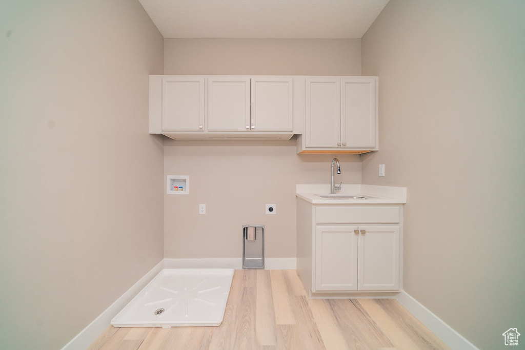 Washroom with hookup for a washing machine, hookup for an electric dryer, light wood-style flooring, baseboards, and cabinet space