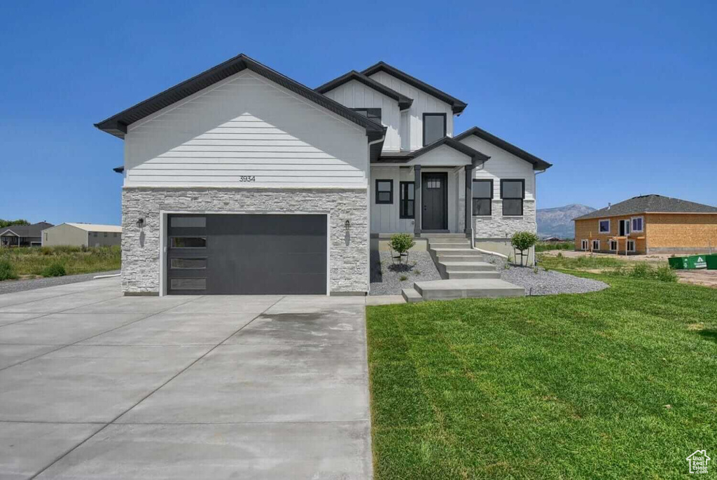 Contemporary house featuring concrete driveway, a front lawn, stone siding, and an attached garage