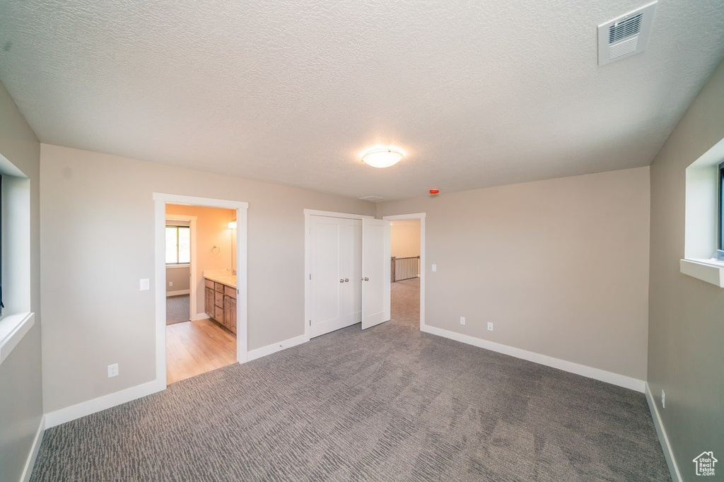 Unfurnished bedroom with carpet flooring, baseboards, a textured ceiling, ensuite bathroom, and a closet