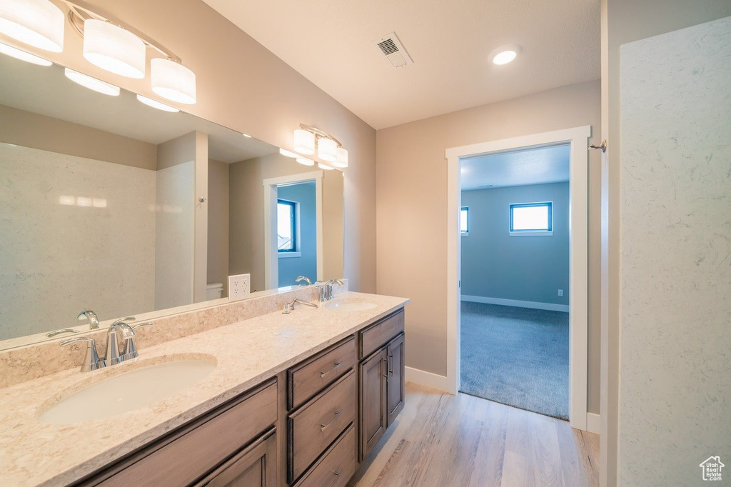Bathroom featuring wood finished floors, double vanity, baseboards, and recessed lighting