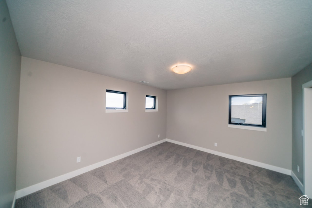 Unfurnished room featuring dark colored carpet, a textured ceiling, and baseboards