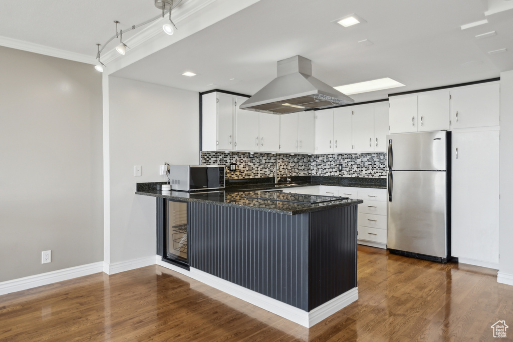 Kitchen featuring stainless steel appliances, island exhaust hood, a peninsula, backsplash, and white cabinetry