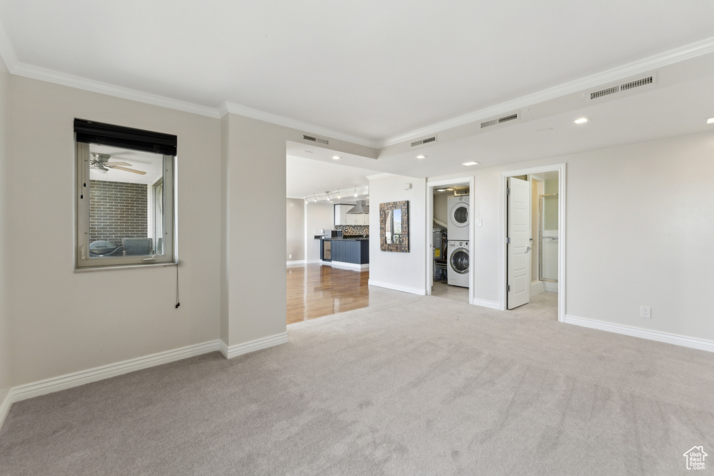 Carpeted empty room featuring stacked washing machine and dryer, crown molding, recessed lighting, and baseboards