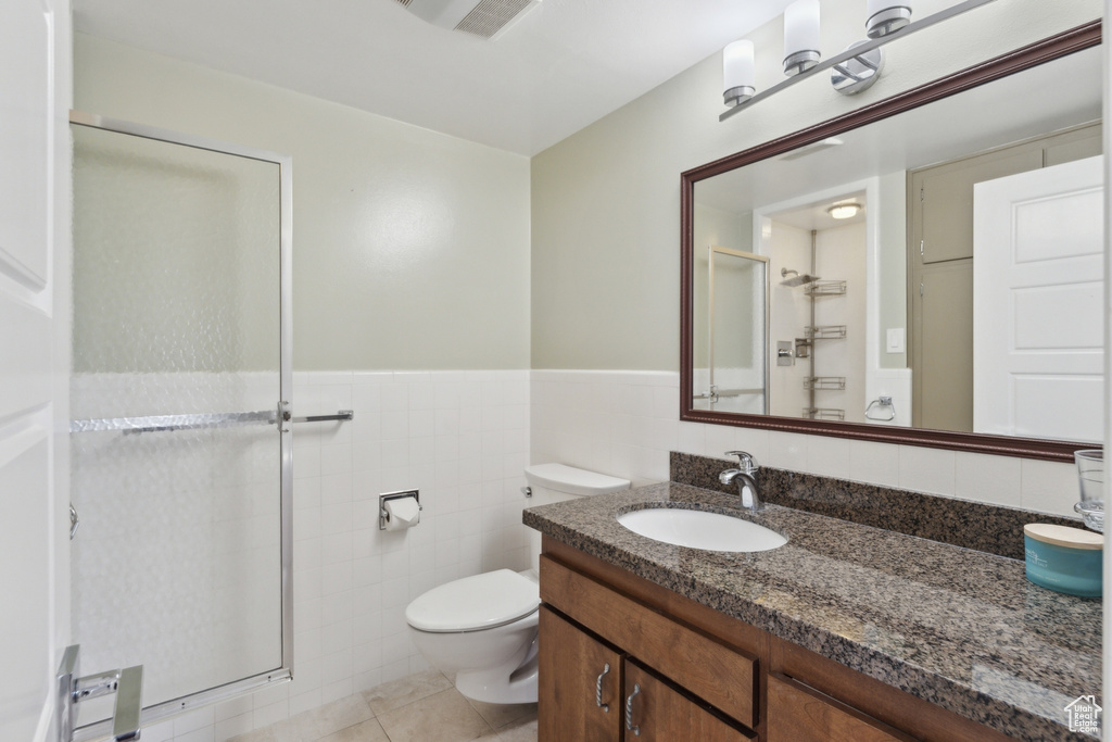Bathroom featuring a stall shower, toilet, tile walls, vanity, and wainscoting