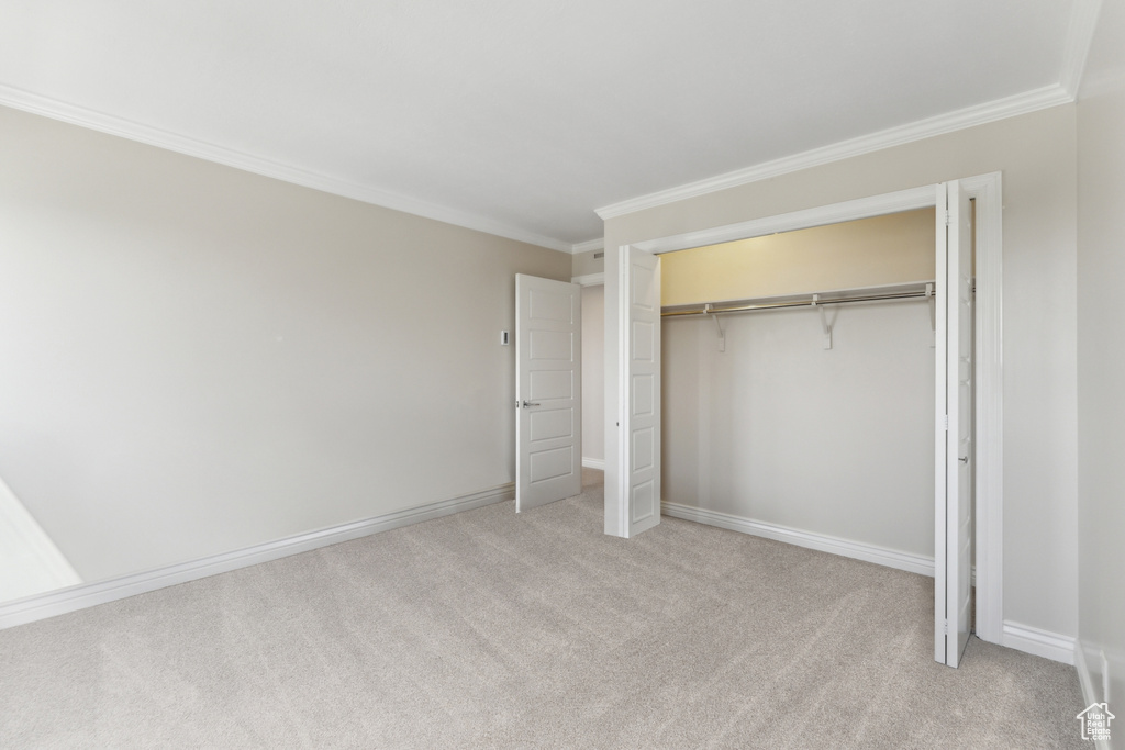 Unfurnished bedroom featuring ornamental molding, light carpet, a closet, and baseboards