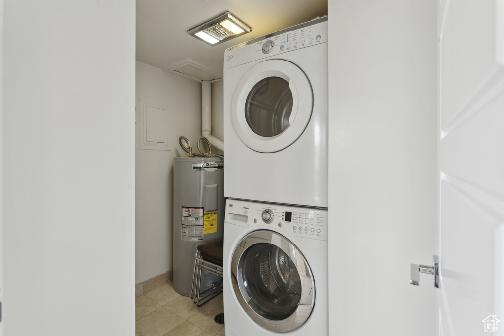 Clothes washing area featuring stacked washer / dryer, water heater, and light tile patterned flooring