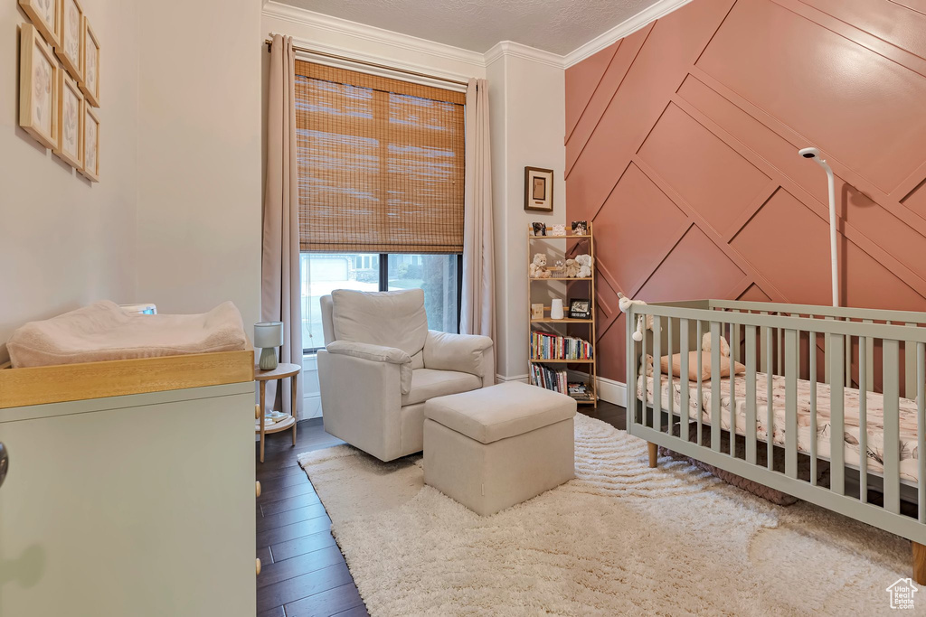 Bedroom featuring a decorative wall, a nursery area, hardwood / wood-style flooring, and crown molding