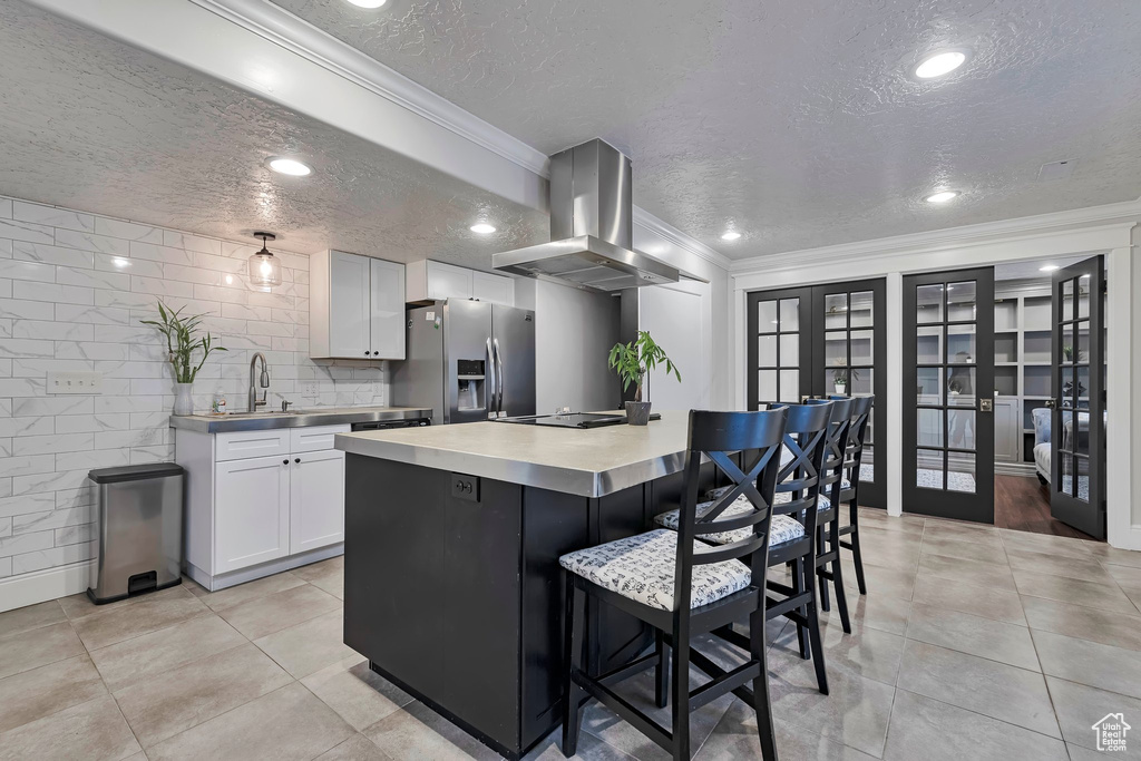 Kitchen featuring island exhaust hood, stainless steel fridge, a textured ceiling, a sink, and white cabinets