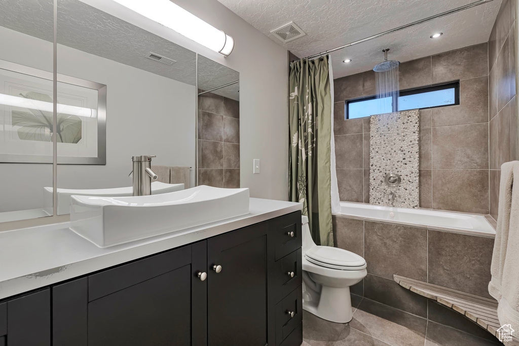 Bathroom featuring tiled shower / bath combo, a textured ceiling, toilet, vanity, and tile patterned floors