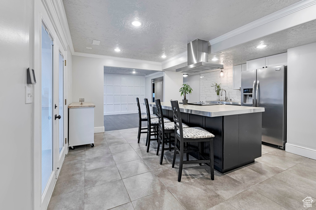 Kitchen with stainless steel fridge, island range hood, ornamental molding, a textured ceiling, and a breakfast bar