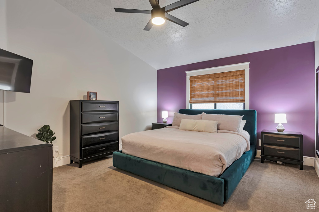 Bedroom with light colored carpet, vaulted ceiling, a textured ceiling, ceiling fan, and baseboards