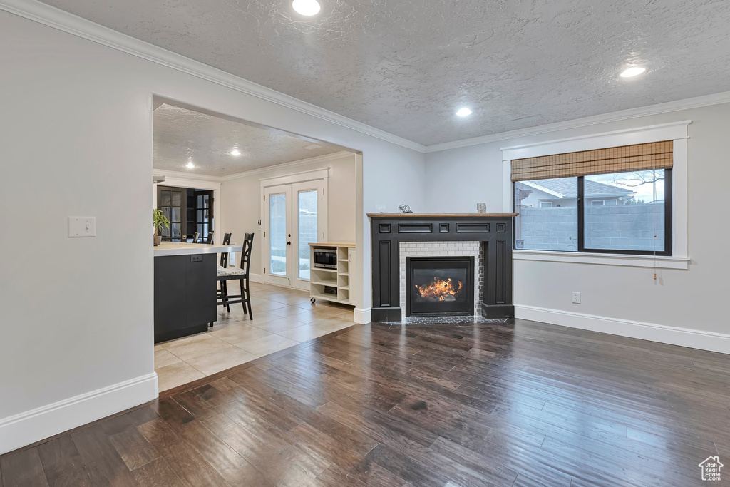 Living area with plenty of natural light, wood finished floors, baseboards, a textured ceiling, and crown molding