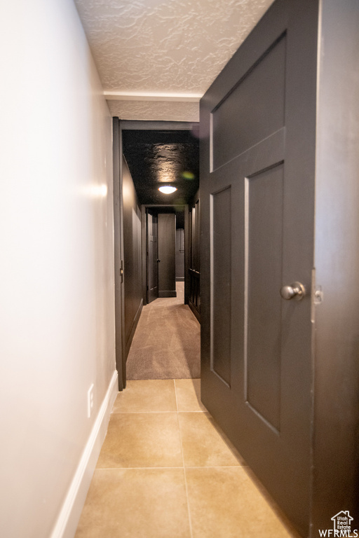 Hallway featuring light tile patterned flooring, baseboards, and a textured ceiling