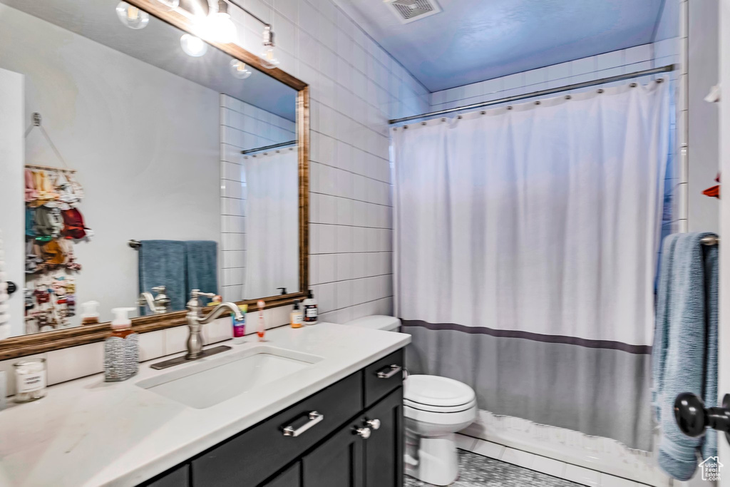 Bathroom featuring tile walls, toilet, vanity, and curtained shower
