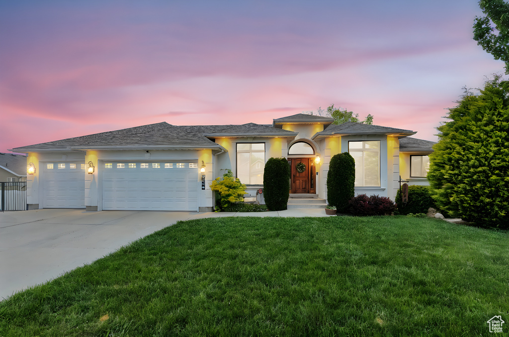 View of front of house with a garage, driveway, a yard, and stucco siding