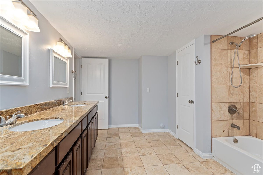 Full bath with baseboards,  shower combination, double vanity, and a textured ceiling