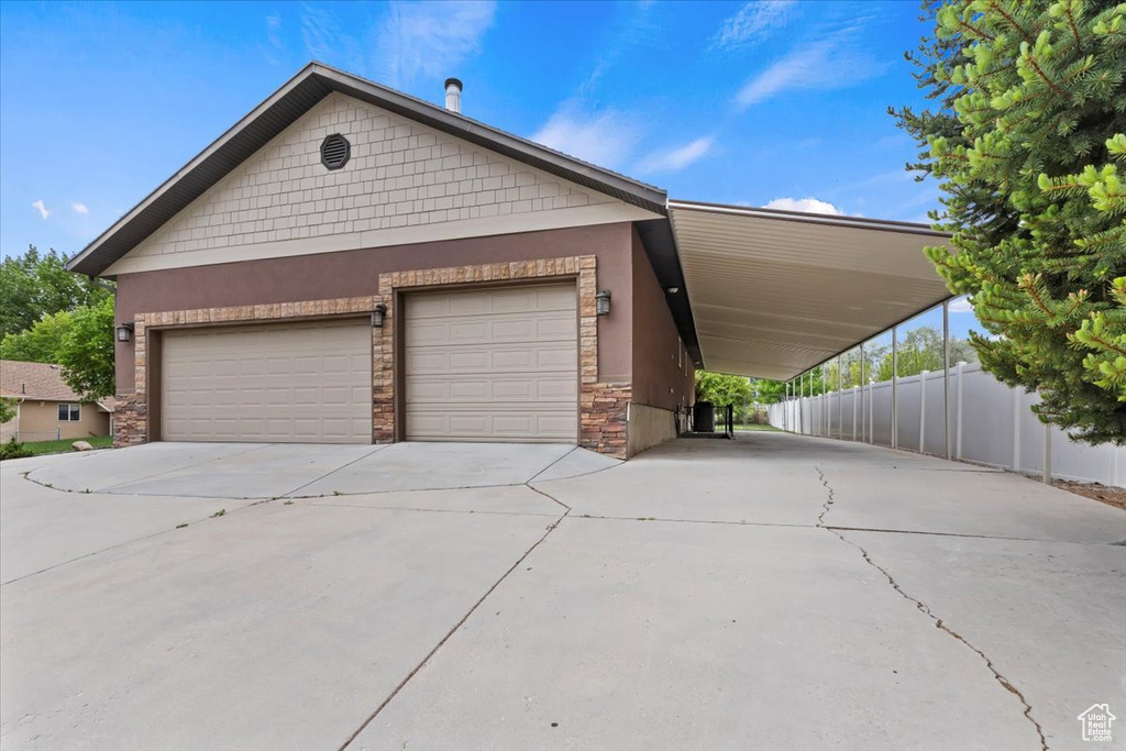 View of front of property with stucco siding, driveway, stone siding, and fence