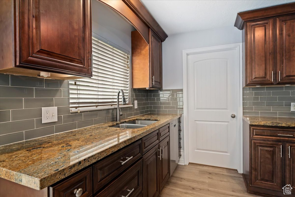 Kitchen featuring a sink, backsplash, light wood finished floors, light stone countertops, and dark brown cabinetry