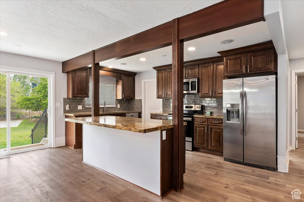 Kitchen with appliances with stainless steel finishes, light wood finished floors, tasteful backsplash, dark brown cabinetry, and a textured ceiling