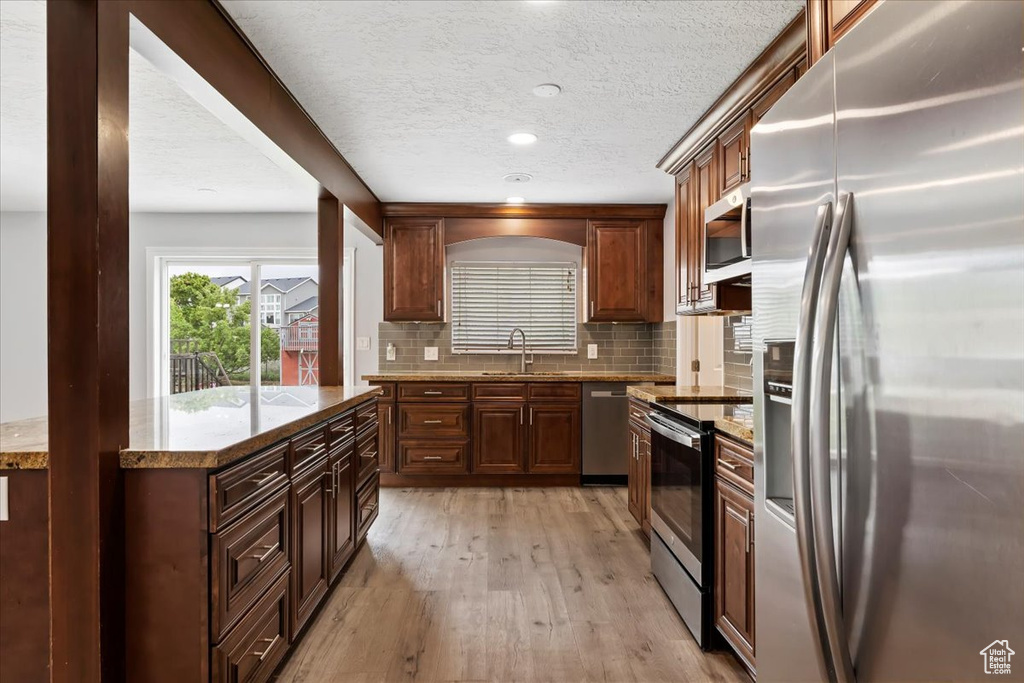 Kitchen with stainless steel appliances, a sink, light wood-type flooring, a textured ceiling, and backsplash