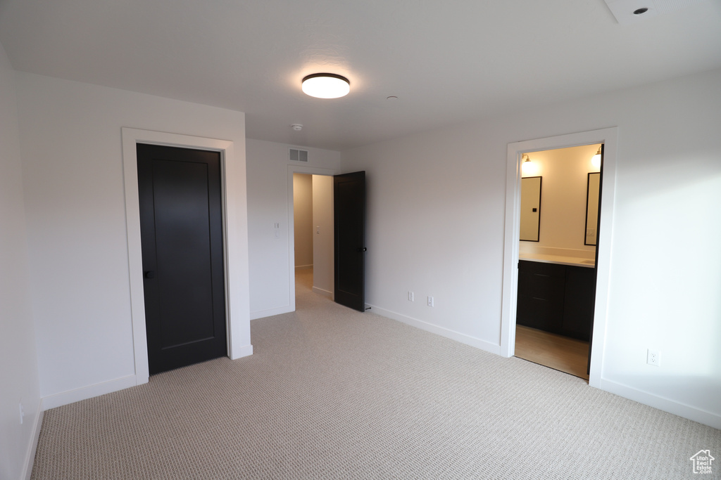 Unfurnished bedroom featuring light colored carpet, baseboards, and connected bathroom