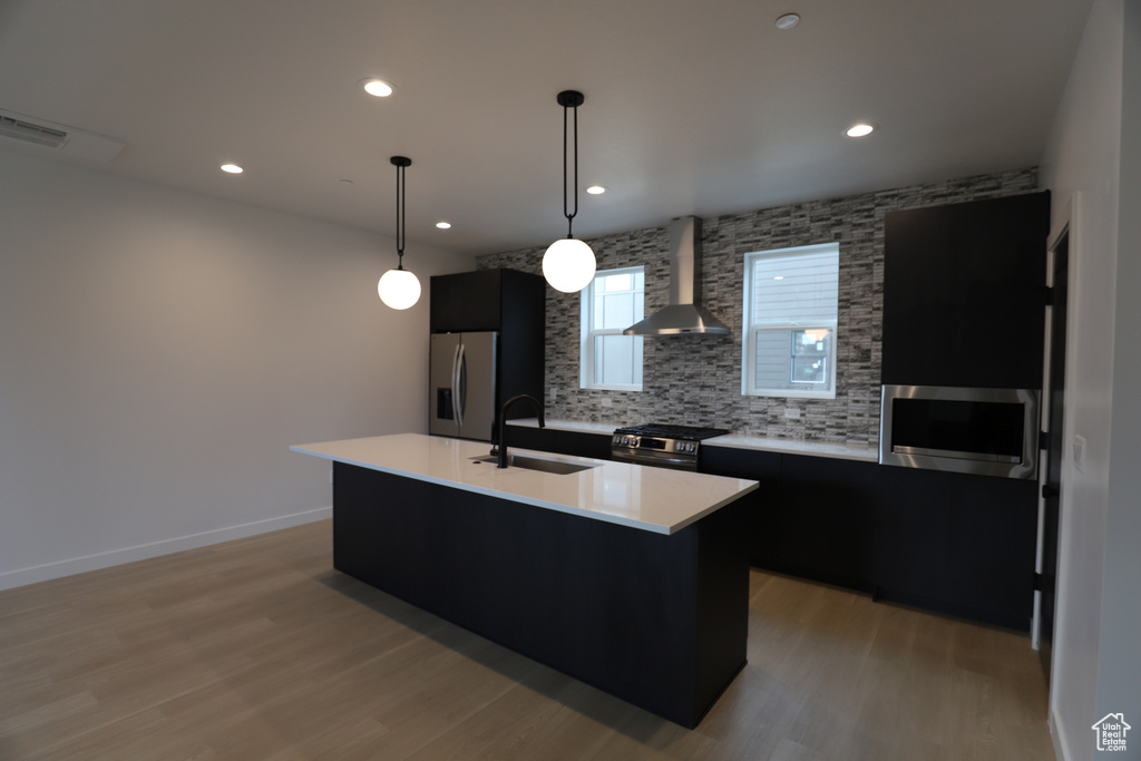 Kitchen featuring wall chimney range hood, appliances with stainless steel finishes, a sink, dark cabinetry, and recessed lighting