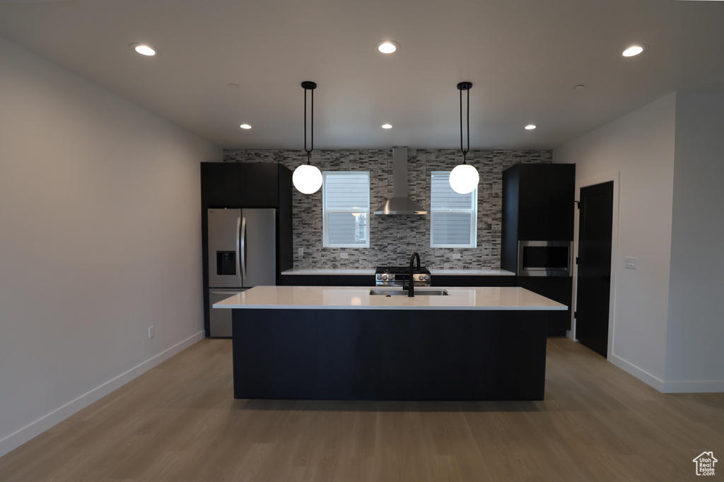 Kitchen featuring stainless steel fridge with ice dispenser, wall chimney range hood, a sink, light countertops, and recessed lighting