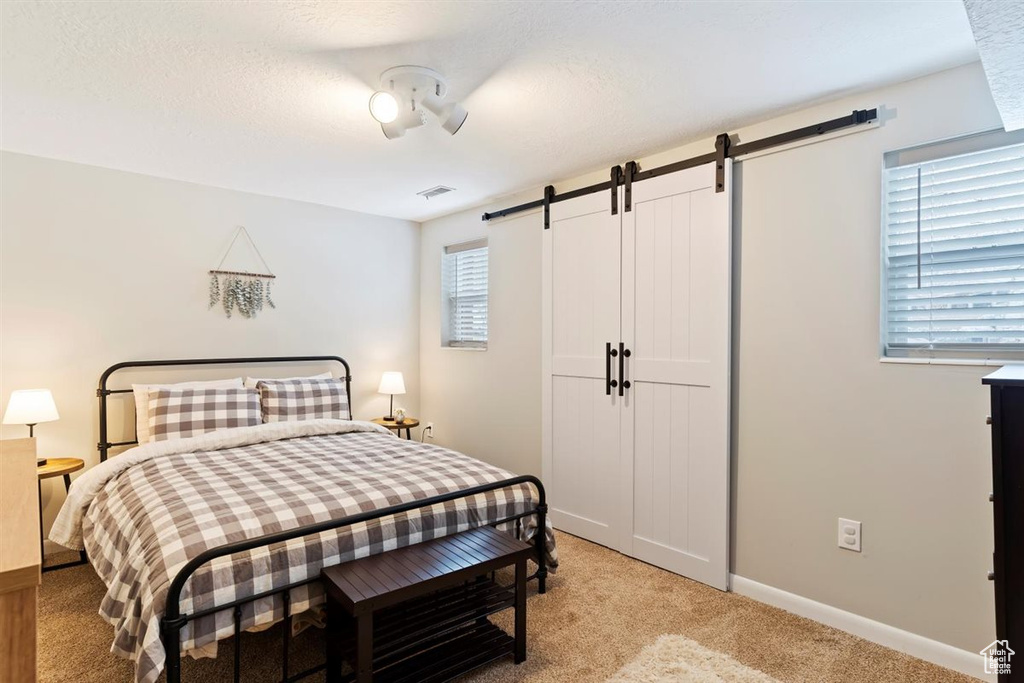 Bedroom featuring a barn door, light carpet, and baseboards