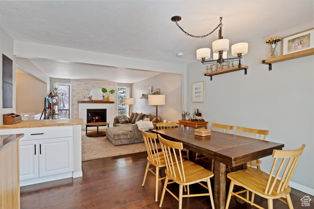 Dining space featuring dark wood-type flooring, a brick fireplace, a chandelier, and baseboards