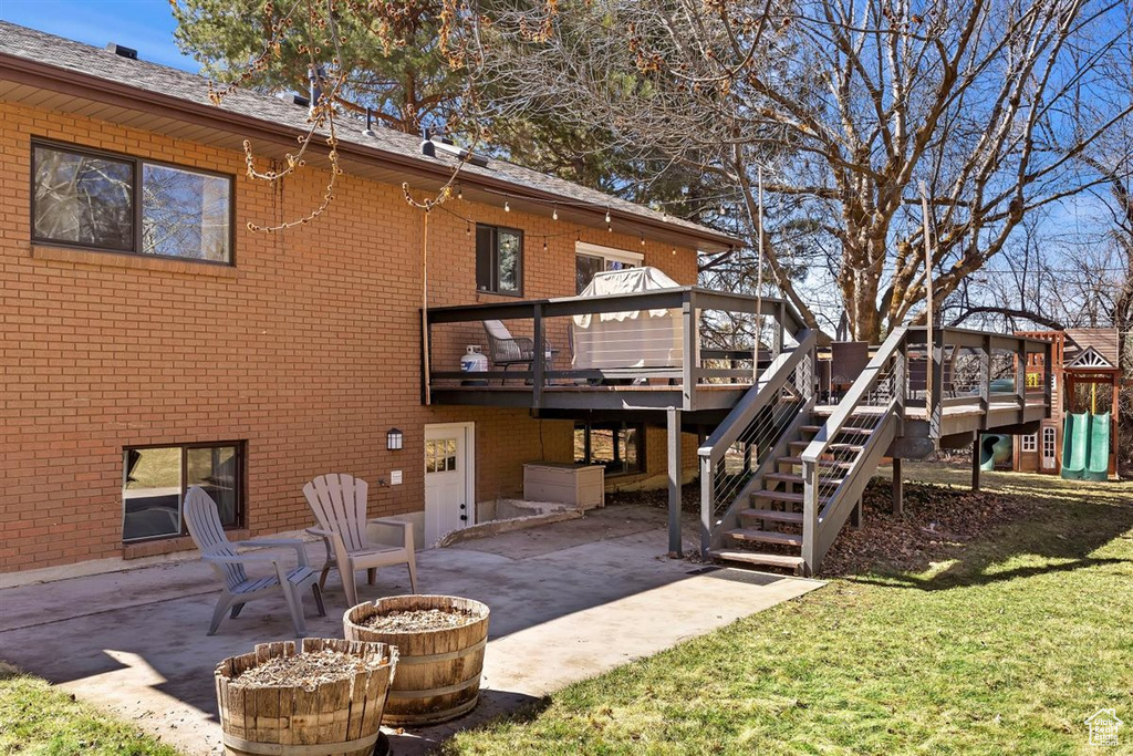 Rear view of property with a patio area, brick siding, a wooden deck, and a lawn