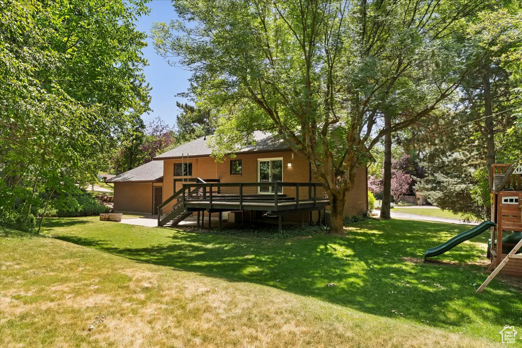 View of grassy yard with a playground, a wooden deck, and stairs