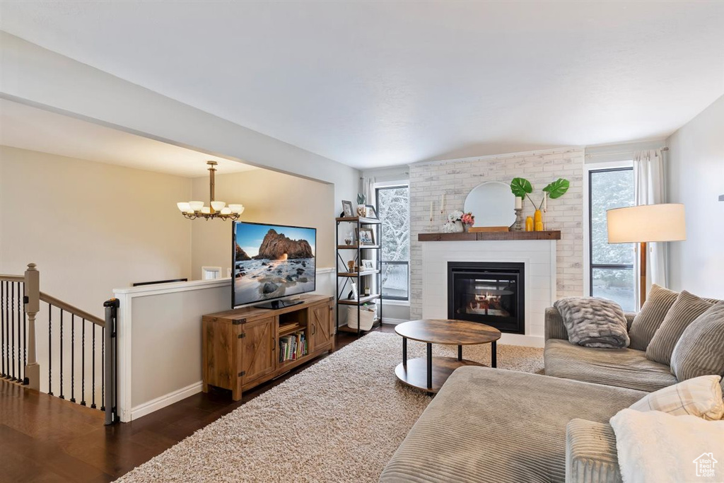 Living room with plenty of natural light, dark wood-style floors, a chandelier, and a brick fireplace