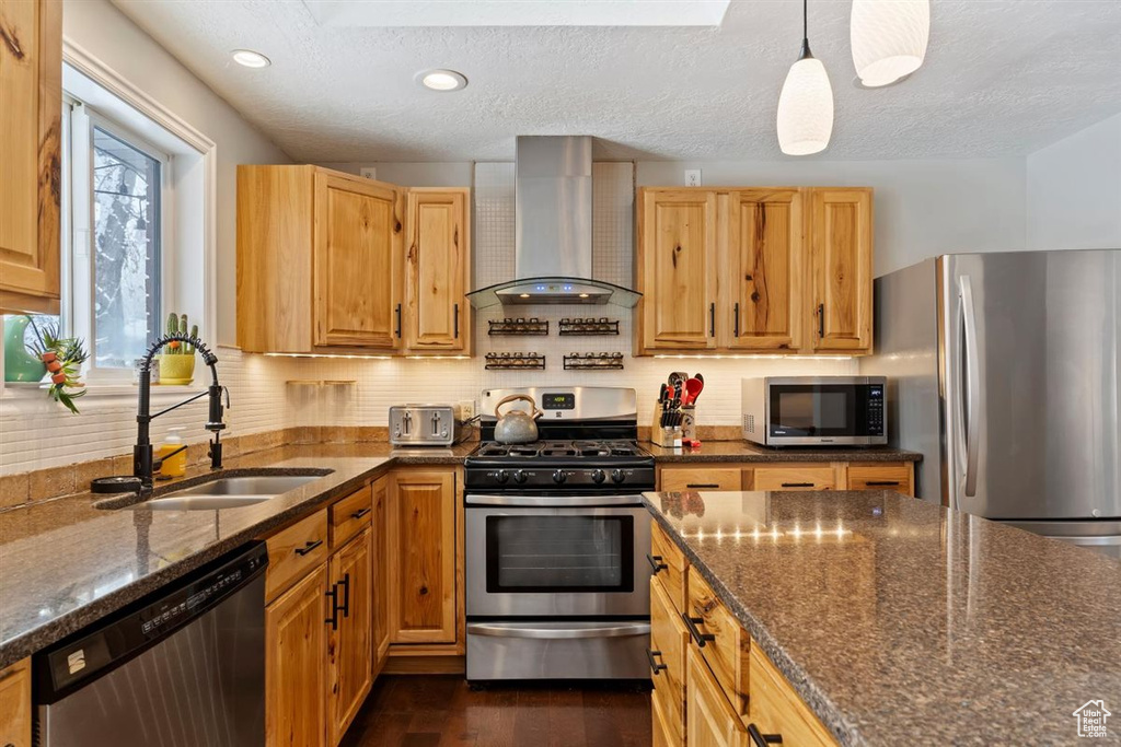 Kitchen with wall chimney range hood, stainless steel appliances, a sink, dark stone counters, and tasteful backsplash