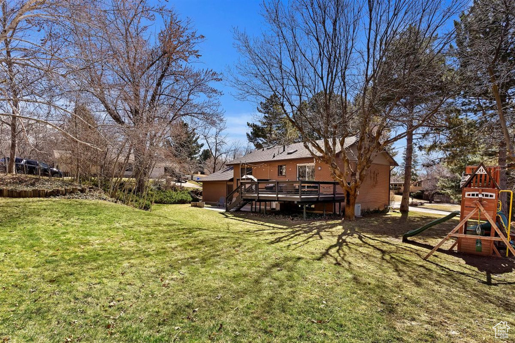 View of grassy yard featuring a deck and a playground