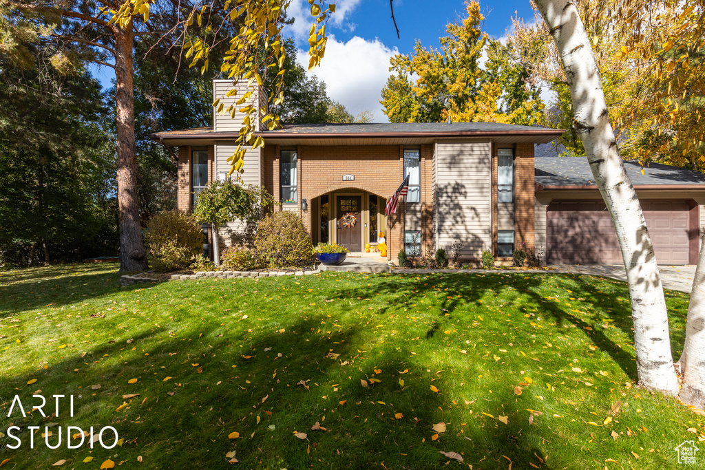 View of front of house with an attached garage, a front lawn, a chimney, brick siding, and driveway